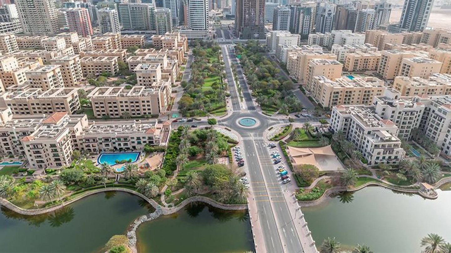 Aerial view of Al Barsha South: low-rise residential buildings, green parks, a lake and a tree-lined road